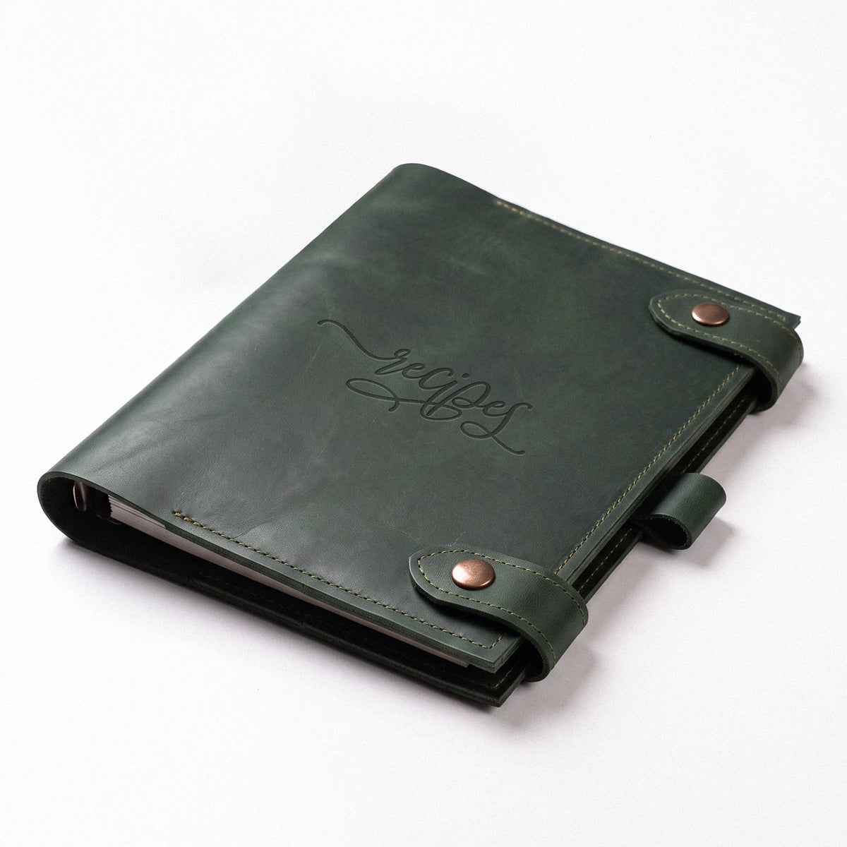 A dark green leather recipe binder with an embossed cursive script logo on the front, secured by a snap strap closure with copper-toned metal snaps, shown on a clean white background.